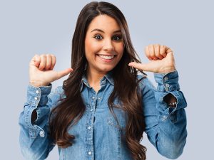 Mulher feliz aponta para si mesma demonstrando que pode pensar em si e atender aos seus desejos, sem esquecer de equilibrar suas necessidades com as dos outros, estabelecendo assim um egocentrismo positivo.