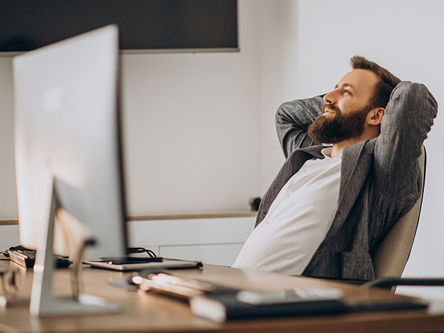 Homem sentado em sua mesa do escritório relaxado pois consegue estabelecer limites saudáveis no trabalho.