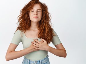 Mulher de olhos fechados e com as mãos no peito, demonstrando que está controlando a respiração para lidar melhor com as crises de ansiedade.